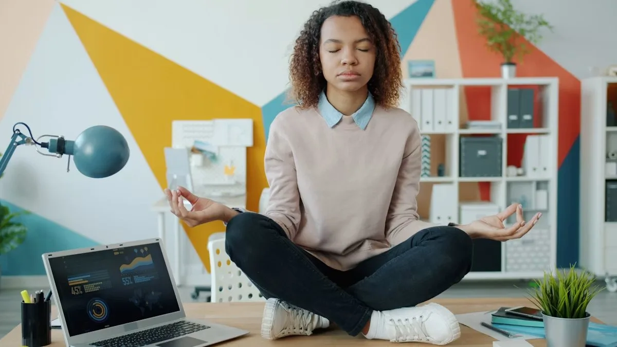 Calm woman meditating at her desk with laptop, illustrating mindfulness as a strategy to set boundaries at work