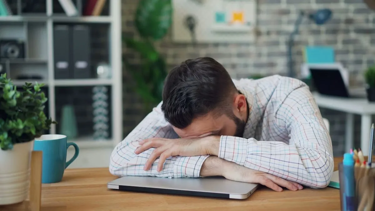 Exhausted man resting head on desk, showing the effects of not setting boundaries at work