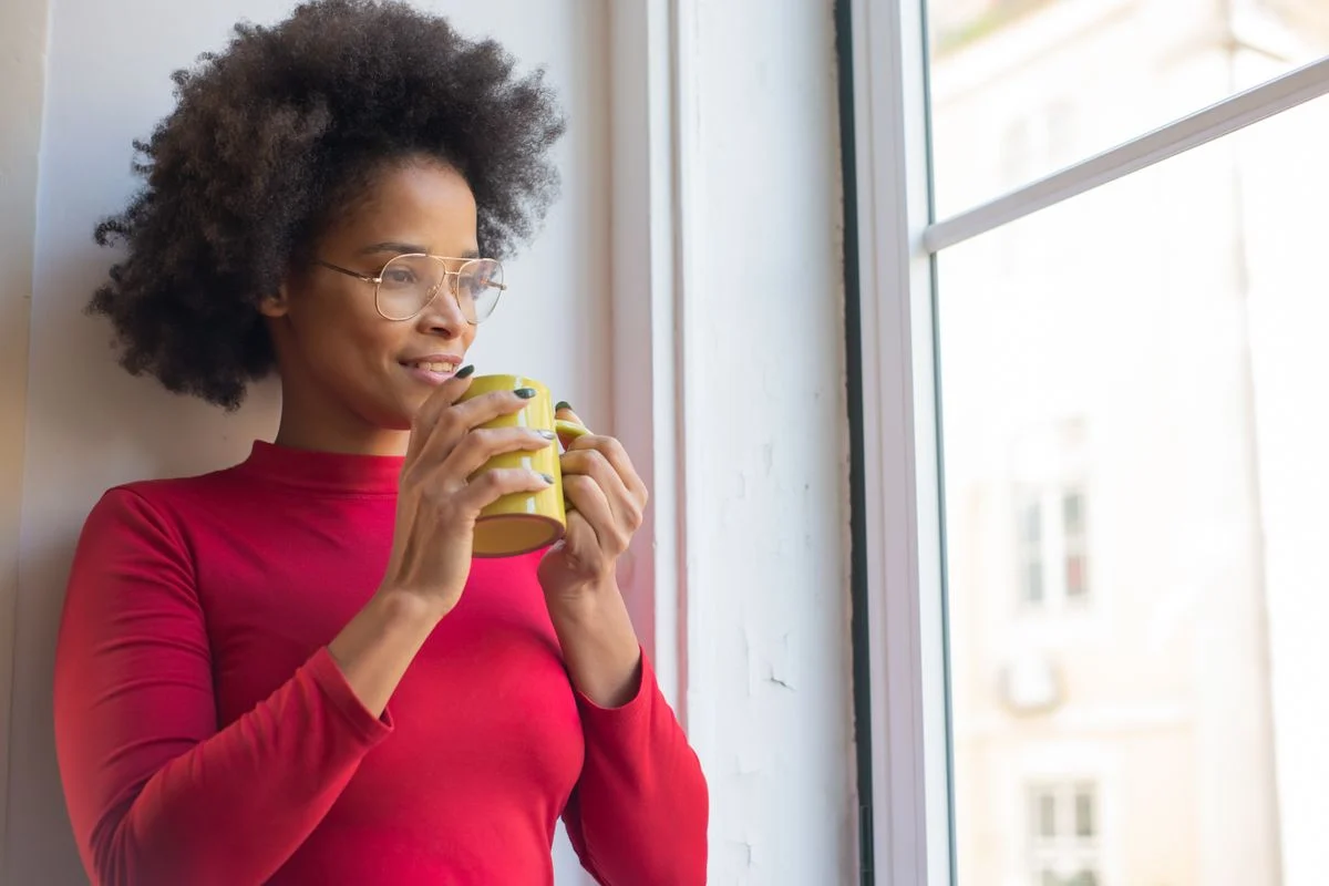 Woman in her late thirties holding a mug and looking out a window, thinking about what to do with her life